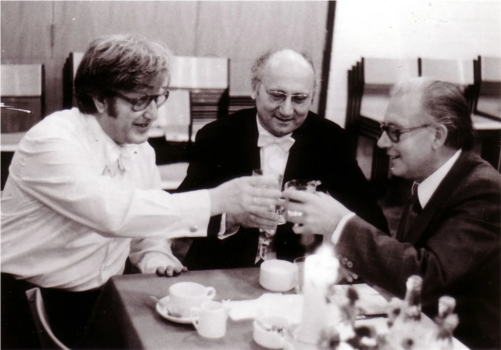 Dietrich von Bausznern, Wolfgang Marschner and Bertold Hummel, dressed in evening wear, clink champagne glasses backstage, 1976