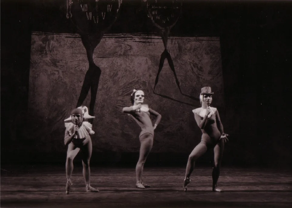 Black-and-white photograph of three dancers in Pierrot costumes, wearing white ruffs and painted masks, against a backdrop featuring two stylised clocks; scene photograph from ‘Die letzte Blume’ (Music: Bertold Hummel, Op. 55a), Würzburg 1975