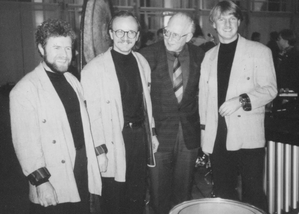 Photo en noir et blanc de trois jeunes musiciens et d'un homme d'âge mûr devant un grand gong, tous posant en vestes claires, en rapport avec l'op. 88d de Bertold Hummel, Stuttgart, 21 novembre 1990